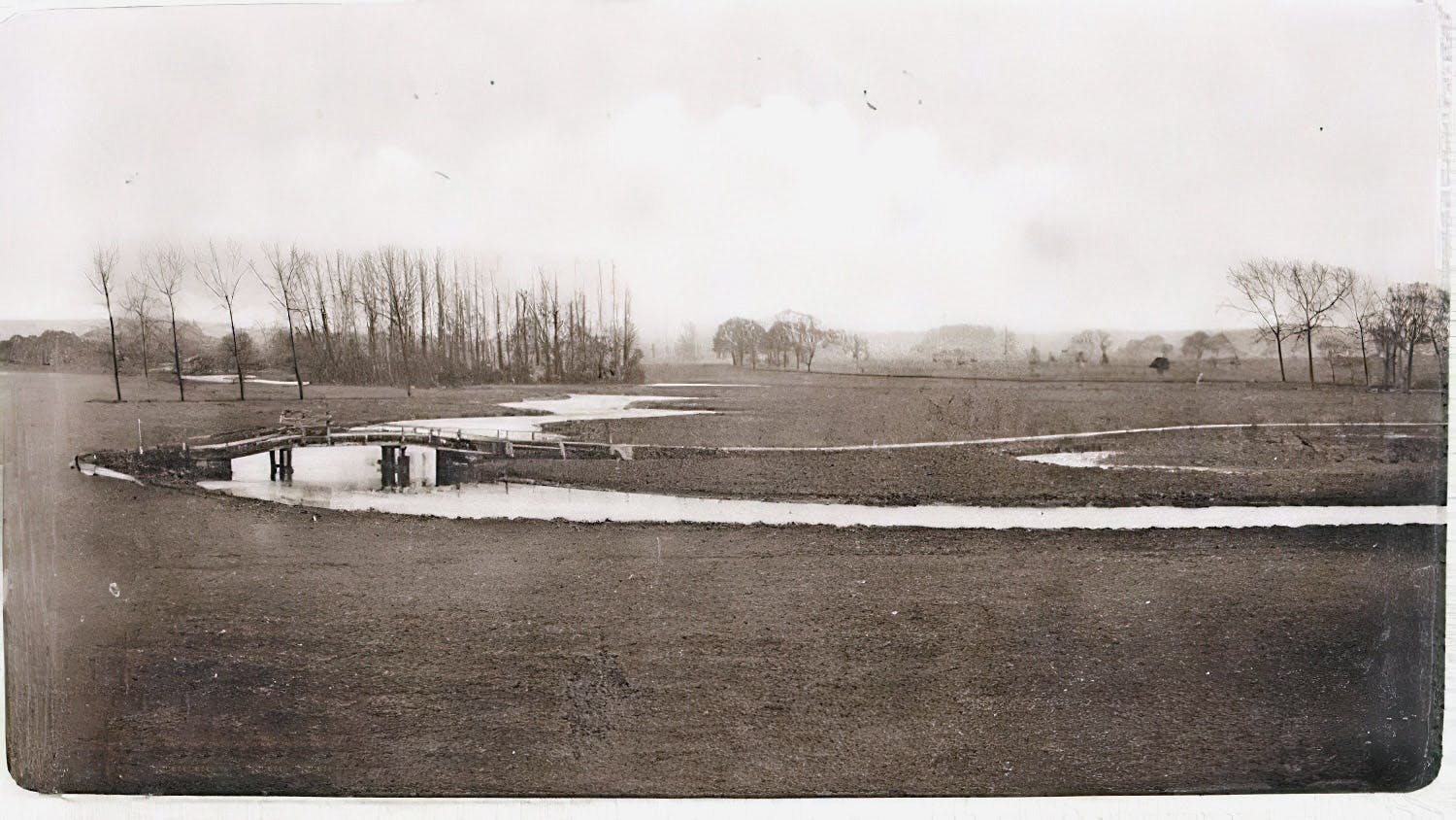 A pre-WW1 view of the bridge taken looking downstream along ‘The Reach’ from the vicinity of Friars Meadow.The photo brings out the meandering nature of the old river course, often the cause of flooding in the low-lying parts of the town. The channel was straightened and meanders cut through after WW2. Before that I the bridge led directly onto the Essex bank, not as today onto an island.